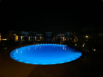 a large blue pool at night with buildings in the background at Lovely first floor tow bed rooms overviewing circular pool for families only in Talabay Aqaba in Aqaba