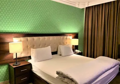 a bedroom with a white bed with a green wall at LANCASTER HOTEL APARTMENTS DAHIET ALRASHEED in Amman