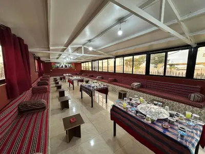 a restaurant with long tables and chairs and windows at Wadi Al-Wala View Camp in Madaba