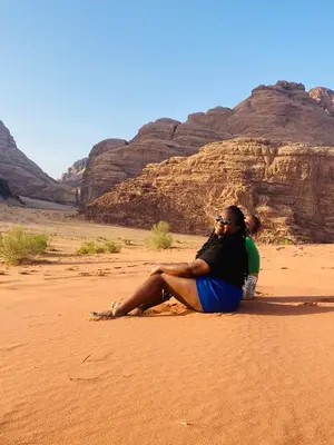 a woman sitting on the sand in the desert at Enjoy Wadi Rum stars in Disah