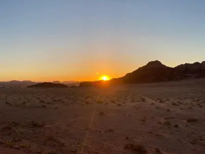 a sunset in the desert with the sun setting at Awad Bedouin camp in Wadi Rum