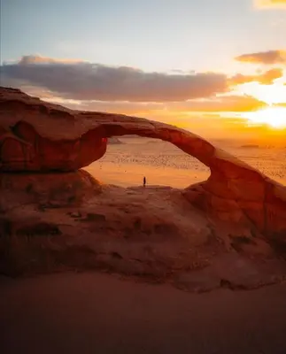 a person standing on the beach under an arch in the sand at Golden sunset luxury camp in Wadi Rum
