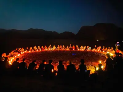 a group of people standing around a circle of lit candles at Wadi rum Rozana camp in Wadi Rum