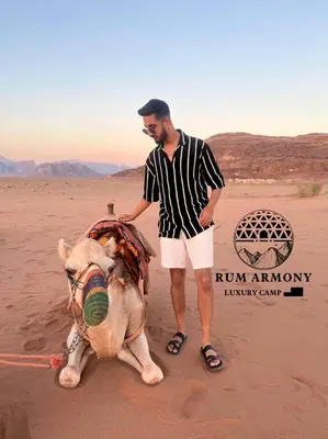 a man standing next to a camel in the desert at Armony rum camp in Wadi Rum