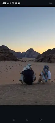 two people sitting on the sand in the desert at Talal Wadi Rum in Wadi Rum