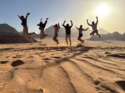 a group of people jumping in the sand on the beach at Talal Wadi Rum in Wadi Rum