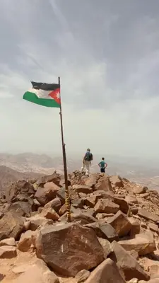 a flag on the top of a rocky mountain at Talal Wadi Rum in Wadi Rum