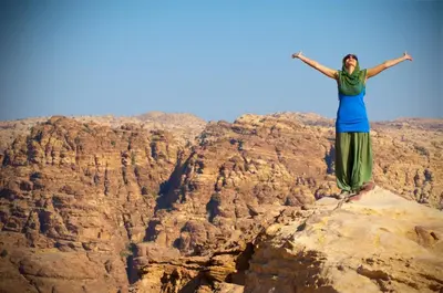a woman standing on top of a cliff with her arms outstretched at Pink city cottage in Wadi Musa