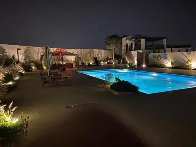a swimming pool at night with chairs and umbrellas at Qaimariya Farmhouse Amman - Day Use - Lodging - Events in Amman