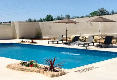 a swimming pool with chairs and umbrellas at Qaimariya Farmhouse Amman - Day Use - Lodging - Events in Amman