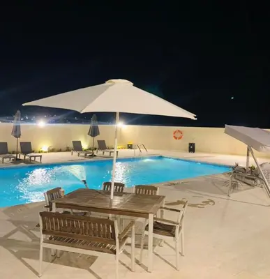 a pool with a table and a large umbrella at Qaimariya Farmhouse Amman - Day Use - Lodging - Events in Amman