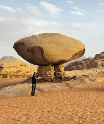 a man standing under a large rock in the desert at Wadi Rum Rose Luxury camp in Wadi Rum