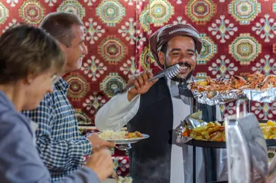 a man is eating food with two people at WhyDesert Camp & Tours in Wadi Rum