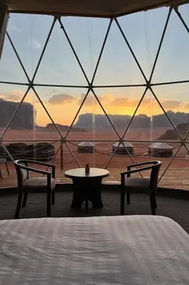 a room with a table and two chairs and a large window at Golden Gate Luxury Camp in Wadi Rum