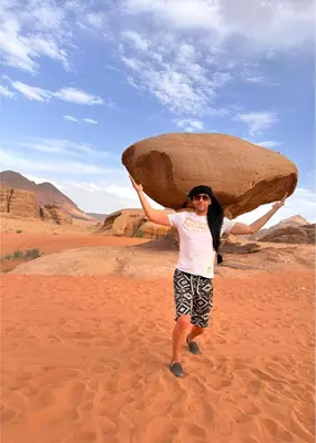 a woman holding up a large rock in the desert at The bubble camp in Wadi Rum