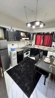 a kitchen with black cabinets and a table in it at شقة مفروشة بغرفتي نوم الجاردنز in Umm Uthainah