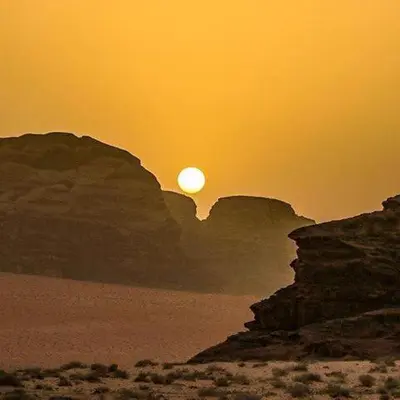 a sunset in the desert with the sun between two mountains at Wadi Rum Time in Wadi Rum
