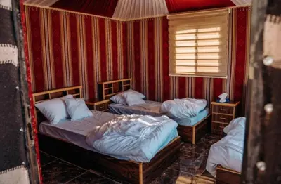 three beds in a room with red walls at Amazing Wadi Rum Camp in Wadi Rum