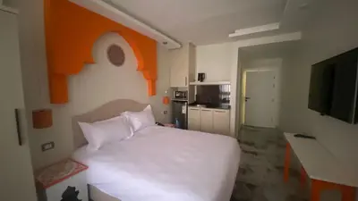 a bedroom with a white bed and an orange wall at Amman Trail Hotel & Studios in Amman
