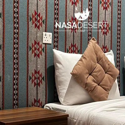 a pillow on a bed with a red and white wallpaper at Nasa desert luxury camp in Wadi Rum