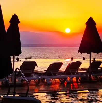 a group of chairs and umbrellas on a beach with the sunset at EP1 TWO BEDROOM APARTMENT AT Samarah Resort in Sowayma