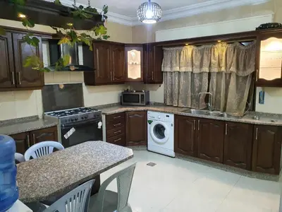 a kitchen with wooden cabinets and a washer and dryer at Noor Apartment in Amman