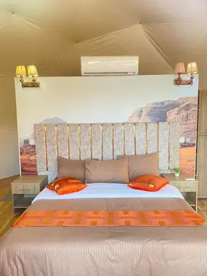 a large bed with two orange pillows in a room at Wadi Rum Desert Tours and Glamping with Hussein in Wadi Rum