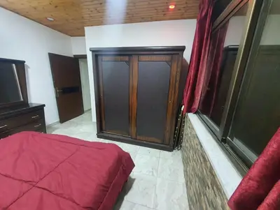a bedroom with a wooden cabinet and a red bed at Maria Apartment in Amman