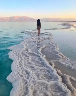 a woman walking through the water on the beach at Tala DeadSea Villa in Sowayma