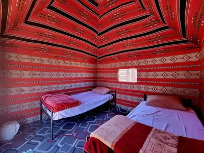 a room with two beds and a red wall at Wadi Rum Backpacker Camp in Wadi Rum
