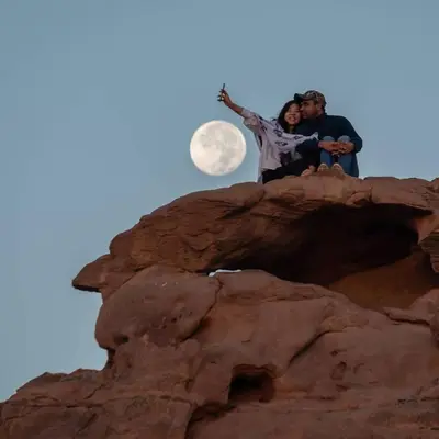 two people sitting on top of a rock with the moon at Moon City Luxury Tent in Wadi Rum