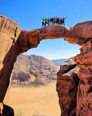 a group of people on horseback standing on an arch in the desert at Faiesal Luxury camp & Tour in Wadi Rum