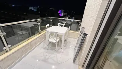 a white table and chairs on a balcony at night at شقق عمو سامي بغرفتين نوم 2 in Amman