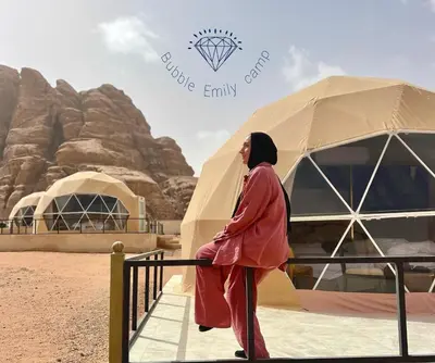 a woman is standing next to a fence in front of tents at Bubble Emily camp in Wadi Rum