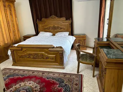 a bedroom with a large wooden bed and a chair at Zahrat AL-Mada'in apartment in Irbid