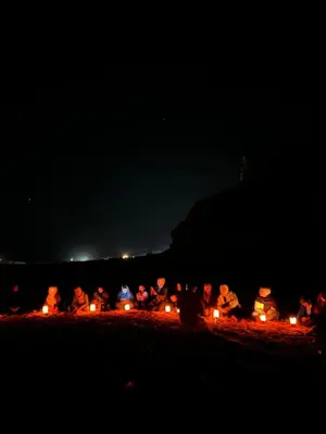 a group of people sitting around a fire at night at Wadi Rum Sarab Camp in Disah