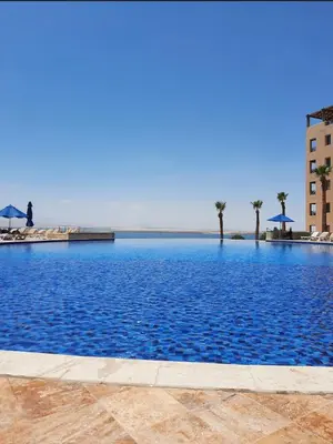 a large pool of blue water with palm trees and umbrellas at Samarah Resort D32 in Sowayma