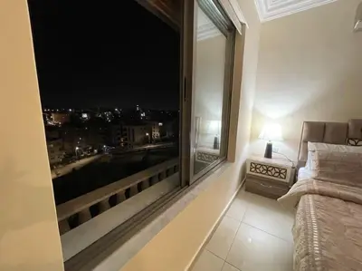 a bedroom with a large window with a view of a city at Sunset Balcony Retreat - Spacious and Comfortable 2 Bedrooms 2 Bathrooms in Amman