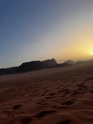 a sunset in the desert with footprints in the sand at Titanic Wadi Rum in Disah