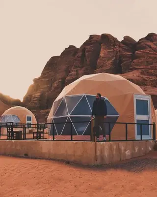 a man standing in front of two tents in the desert at Diamond luxury rum in Wadi Rum