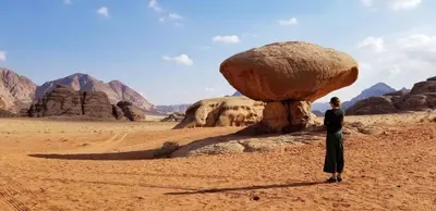 a man standing next to a large rock in the desert at Msek wadi rum camp in Disah