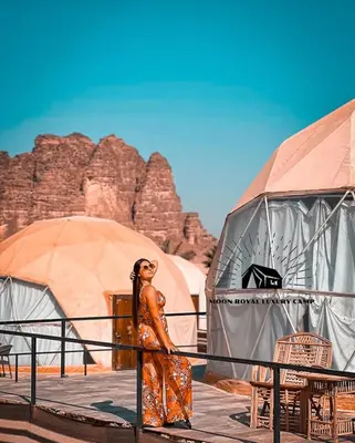 a woman standing next to a fence in front of tents at ROYAL MOON BUBBLES lUXURY CAMP in Wadi Rum
