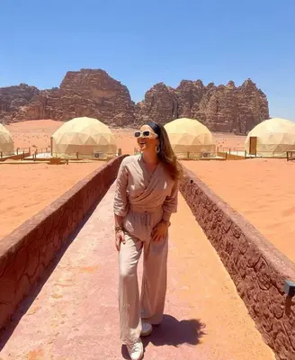 a woman standing next to a wall in the desert at وادي رم in Disah