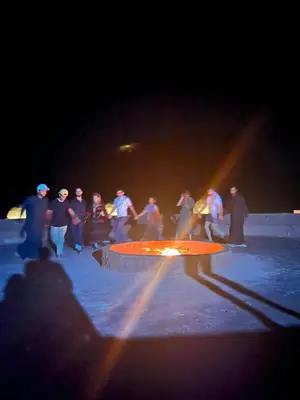 a group of people standing around a fire pit at night at Royal Dunes Camp in Wadi Rum