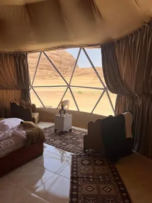 a bedroom with a bed and a large window at Royal Dunes Camp in Wadi Rum