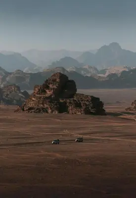 two cars in a field with mountains in the background at RUM YANAL lUXURY CAMP in Wadi Rum