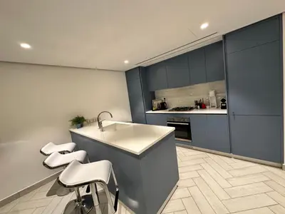 a kitchen with a sink and four stools at Ayla Apartment in Aqaba
