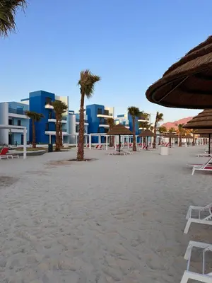 a beach with chairs and palm trees and buildings at Chic One-Bedroom with Sea View in Aqaba