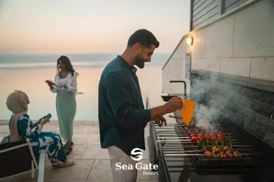 a man cooking food on a grill with a woman at Sea Gate Resort in Sowayma