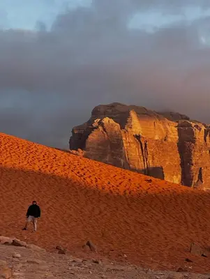 a man walking along a red brick wall in front of a mountain at Wadi rum magical in Wadi Rum